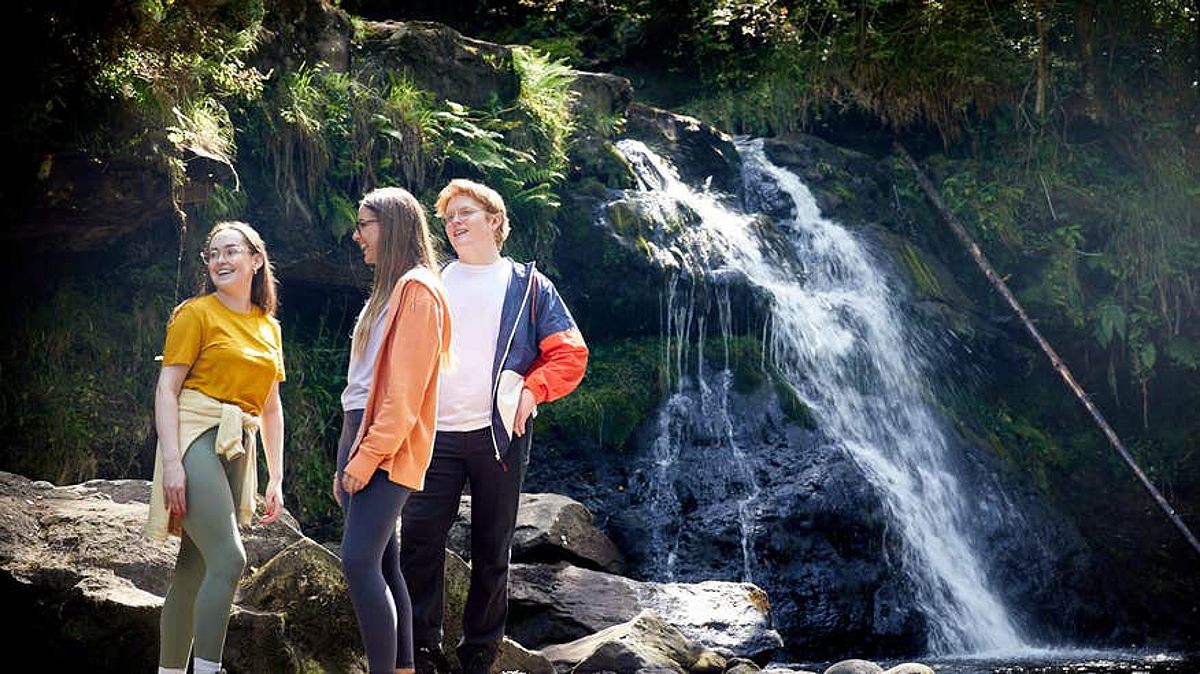 Friends standing beside a waterfall on the Glenbarrow Eco Walk