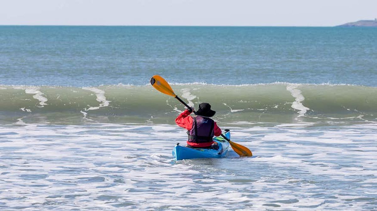 Pictures a sea-kayaker, paddling towards a coming wave on Garrylucas Beach, Kinsale.