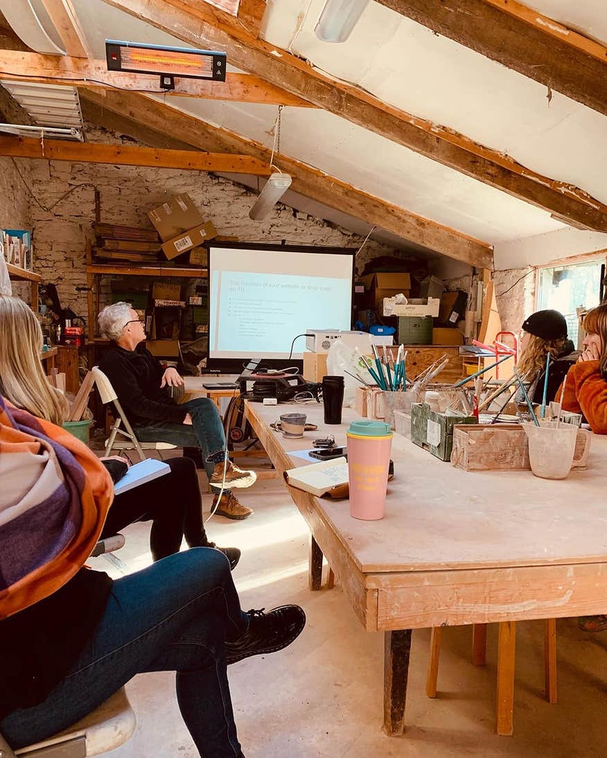 Pottery class at Kinsale Pottery and Arts Centre. A group of people sit around a wooden table while watching a projector screen.