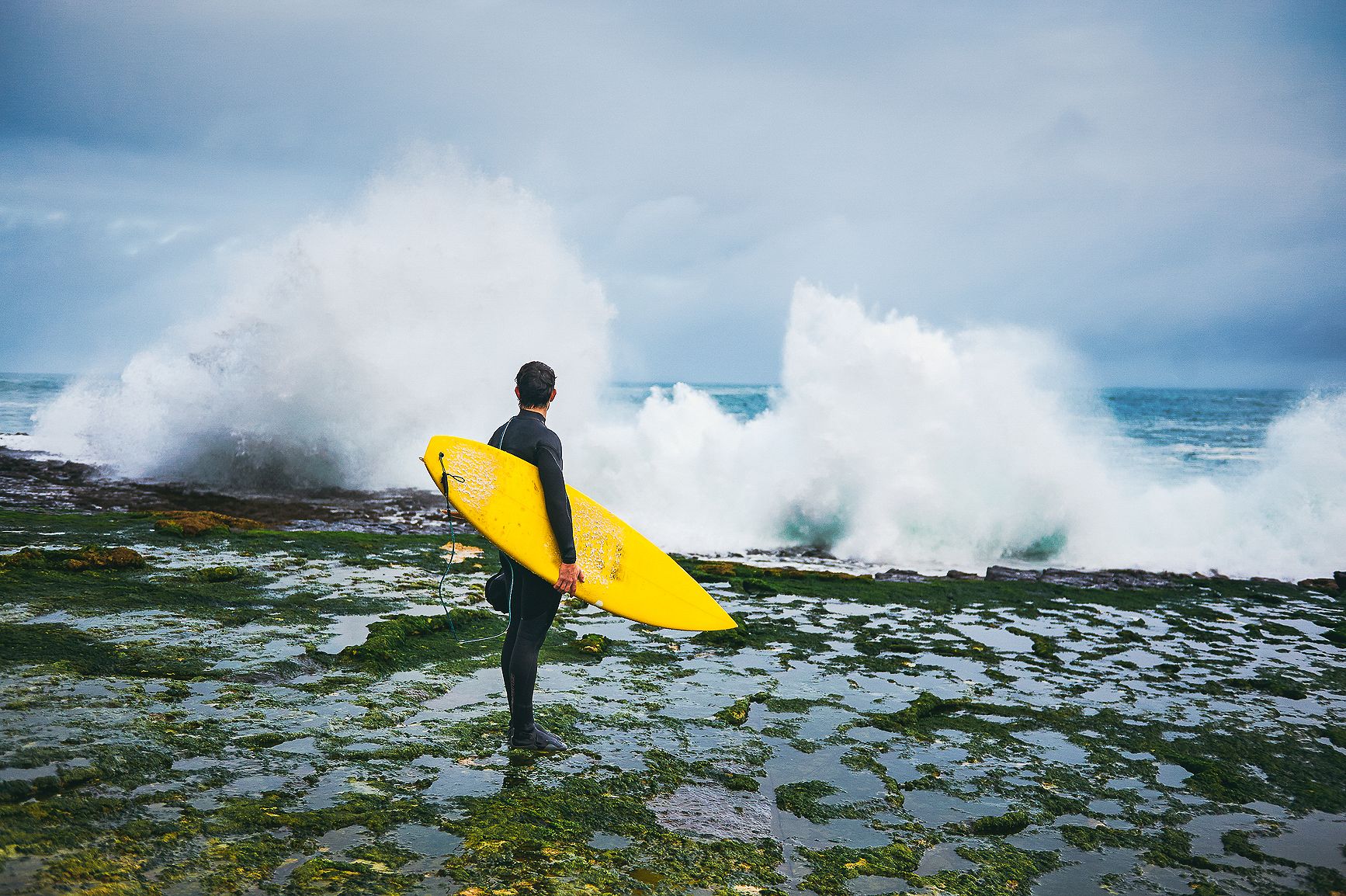 Surfer in a full wet suit looking out at the waves